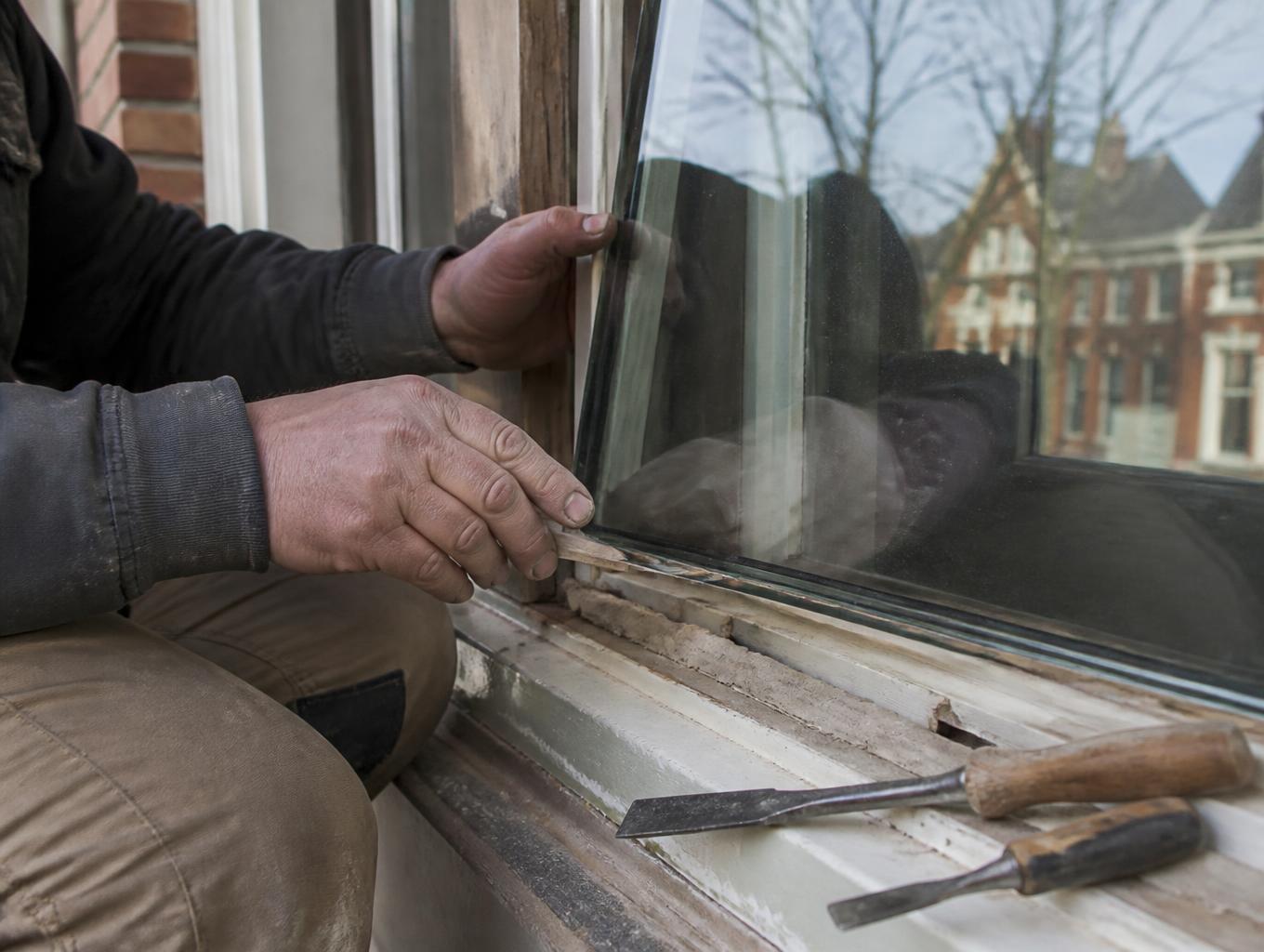 Vakman plaatst een HR++ glaspaneel in de houten sponning van een raamkozijn